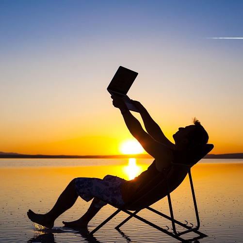 Silhoutette of man on a beach, holding laptop in the air