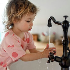 Female toddler washes her hands under an old-fashioned tap